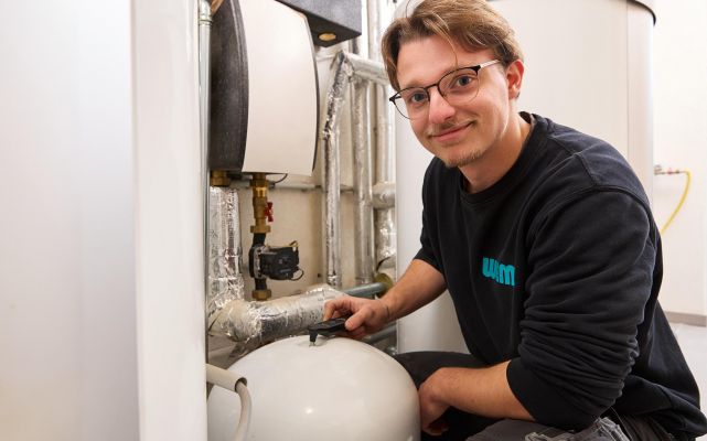 Auszubildender von WEME Heizung & Sanitär prüft eine Heizungsanlage, arbeitet an einem Druckbehälter in einem Technikraum mit Rohrleitungen