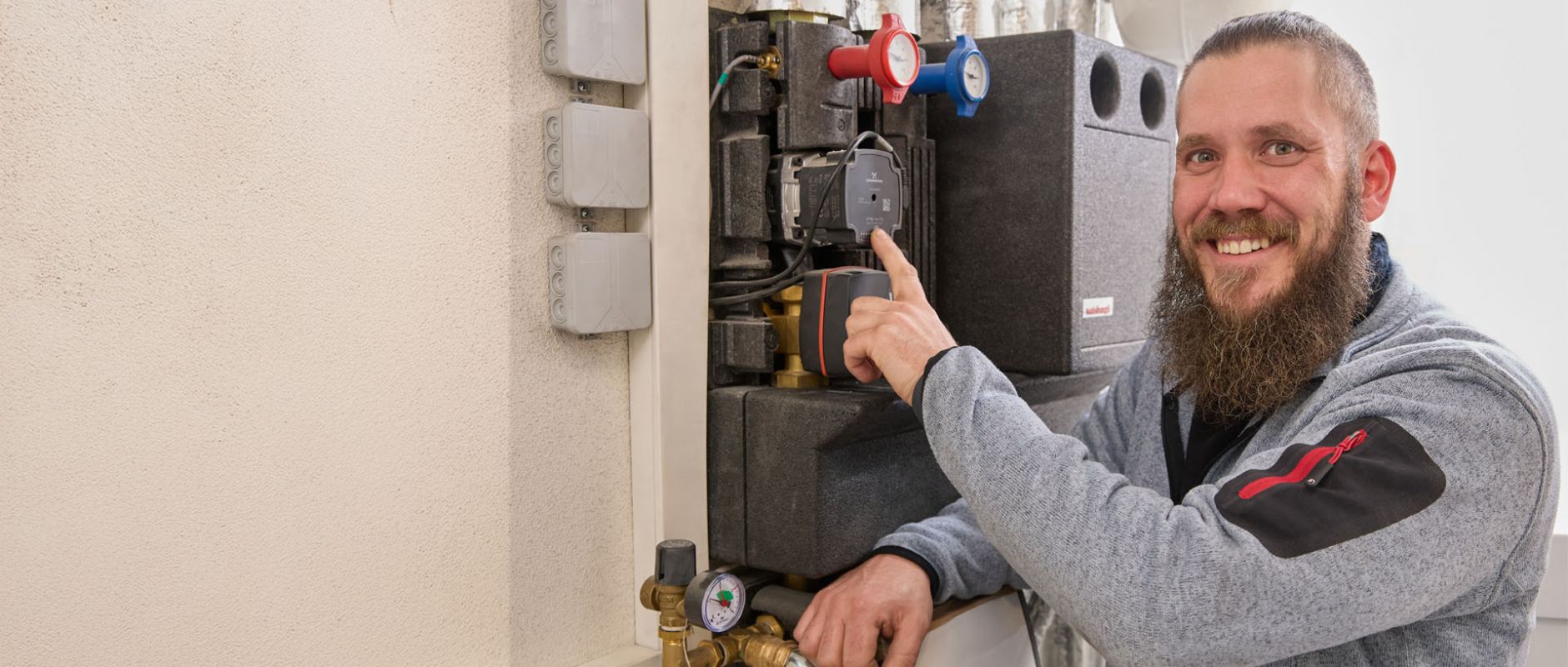 SHK-Fachhandwerker von WEME Heizung & Sanitär steht an einer Heizungsanlage, zeigt auf eine Umwälzpumpe und Armaturen in einem Technikraum