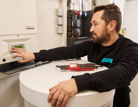 SHK-Fachhandwerker von WEME Heizung & Sanitär bedient die Steuerung einer Heizungsanlage, prüft Einstellungen an einem Heizgerät in einem Technikraum