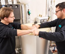 Zwei SHK-Fachhandwerker von WEME Heizung & Sanitär arbeiten gemeinsam an einem Warmwasserspeicher, führen Service- und Reparaturarbeiten im Technikraum durch