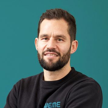 Geschäftsführer Mario Lentes von WEME Versorgungstechnik steht vor petrolfarbenem Hintergrund, trägt schwarze Arbeitskleidung mit WEME-Logo