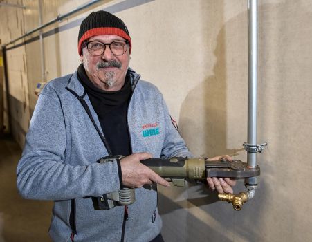 Mitarbeiter der Versorgungstechnik montiert eine Rohrverbindung mit einem Elektrowerkzeug in einem Technikraum