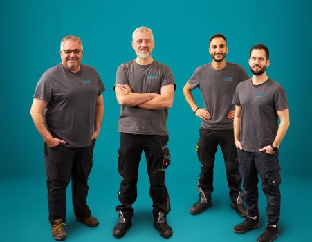 Vier Geschäftsführer des WEME Heizung & Sanitär Teams vor petrolfarbenem Hintergrund, Handwerksprofis im SHK-Bereich präsentieren sich freundlich und professionell