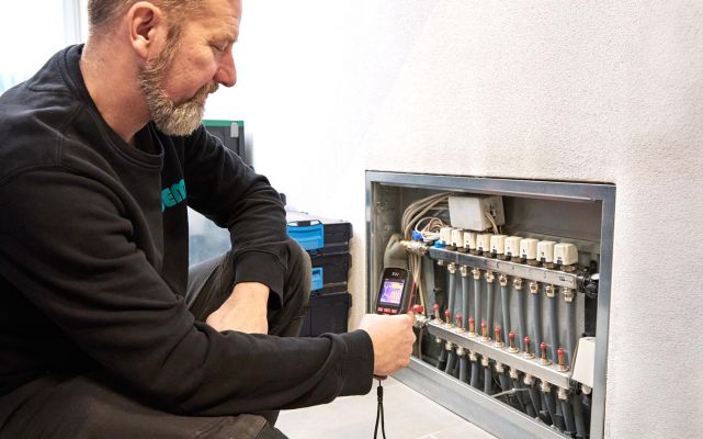 SHK-Fachhandwerker von WEME Heizung & Sanitär überprüft einen Heizkreisverteiler mit einer Wärmebildkamera, Diagnose einer Fußbodenheizung im Technikraum