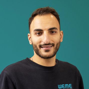 Geschäftsführer Mohammed El-Omar von WEME Versorgungstechnik steht vor petrolfarbenem Hintergrund, trägt schwarze Arbeitskleidung mit WEME-Logo
