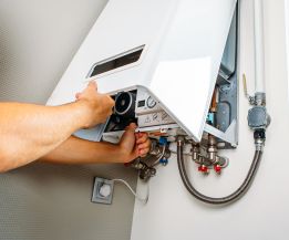 Ein Monteur öffnet und prüft eine wandhängende Gasheizung, sichtbare Anschlüsse und Bedienelemente während einer Heizungswartung