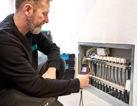 SHK-Fachhandwerker von WEME Heizung & Sanitär überprüft einen Heizkreisverteiler mit einer Wärmebildkamera, Diagnose einer Fußbodenheizung im Technikraum