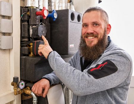 Mitarbeiter der Versorgungstechnik steht an einer Heizungsanlage und überprüft eine Umwälzpumpe in einem Technikraum