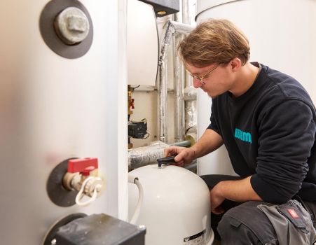 Ein WEME-Mitarbeiter prüft eine Heizungsanlage und misst Komponenten am Warmwasserspeicher im Rahmen einer Beratung zum Heizungsaustausch