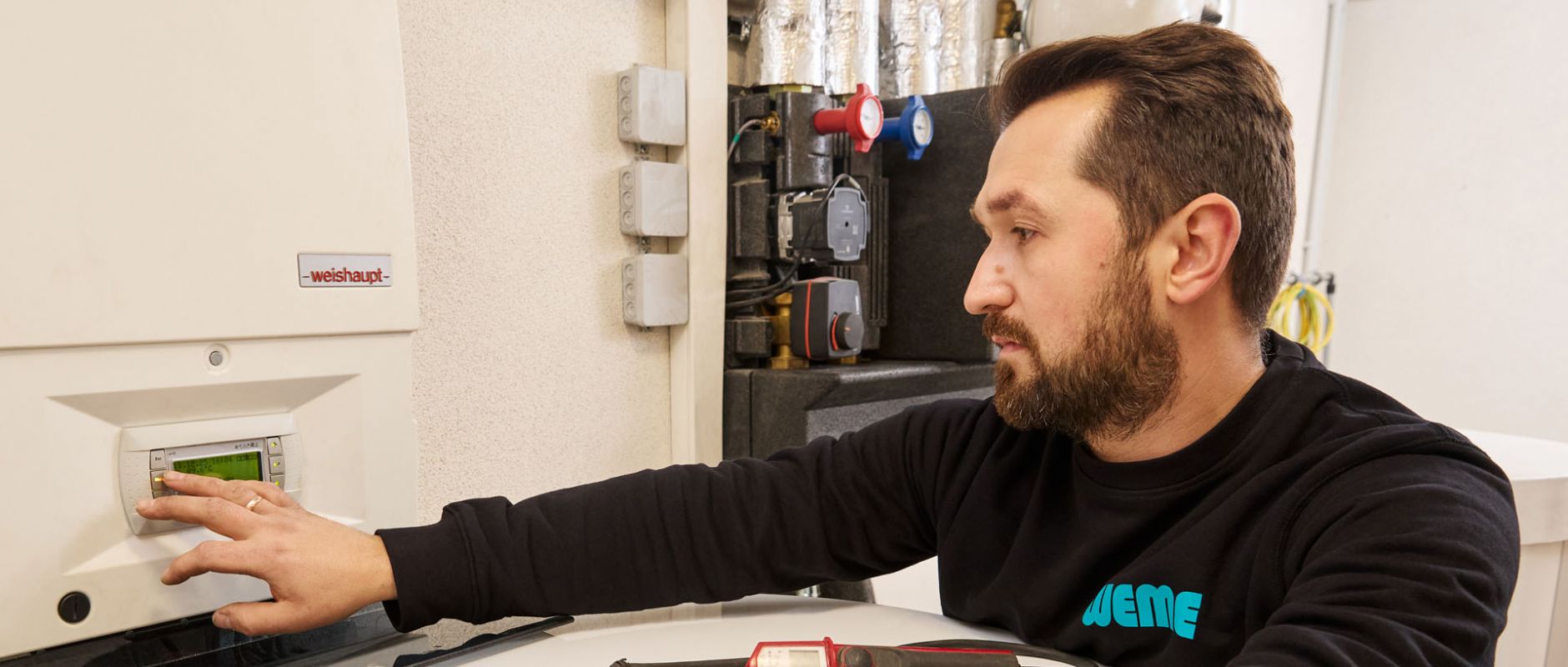 SHK-Fachhandwerker von WEME Heizung & Sanitär bedient die Steuerung einer Heizungsanlage, prüft Einstellungen an einem Heizgerät in einem Technikraum